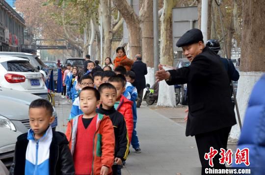 今年69岁的张善德是该校的家长志愿者，每日在学校门前引导来往车辆、向小学生们鞠躬问好、保护孩子安全已经一年有余。　郝学娟 摄